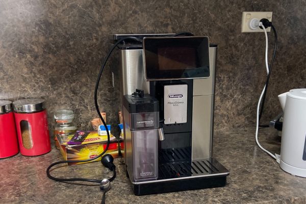A DeLonghi PrimaDonna Soul coffee machine sits on a kitchen bench, plugged in and ready for use. Surrounding the unit are kitchen essentials like a kettle, jars, and coffee pods. This image highlights the type of small kitchen appliances expertly serviced by Quality Appliance Repairs (QAR), including premium espresso machines.