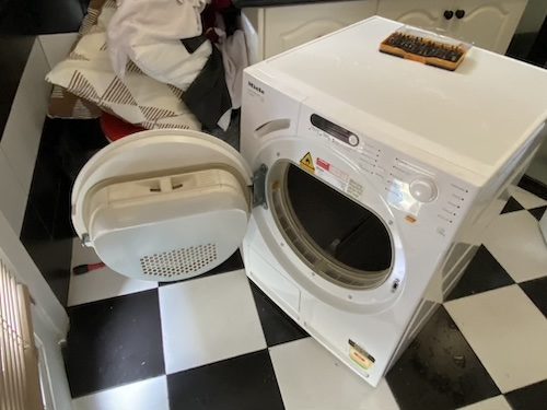 Front-loading washing machine with open door in a Brisbane laundry, needing repair.