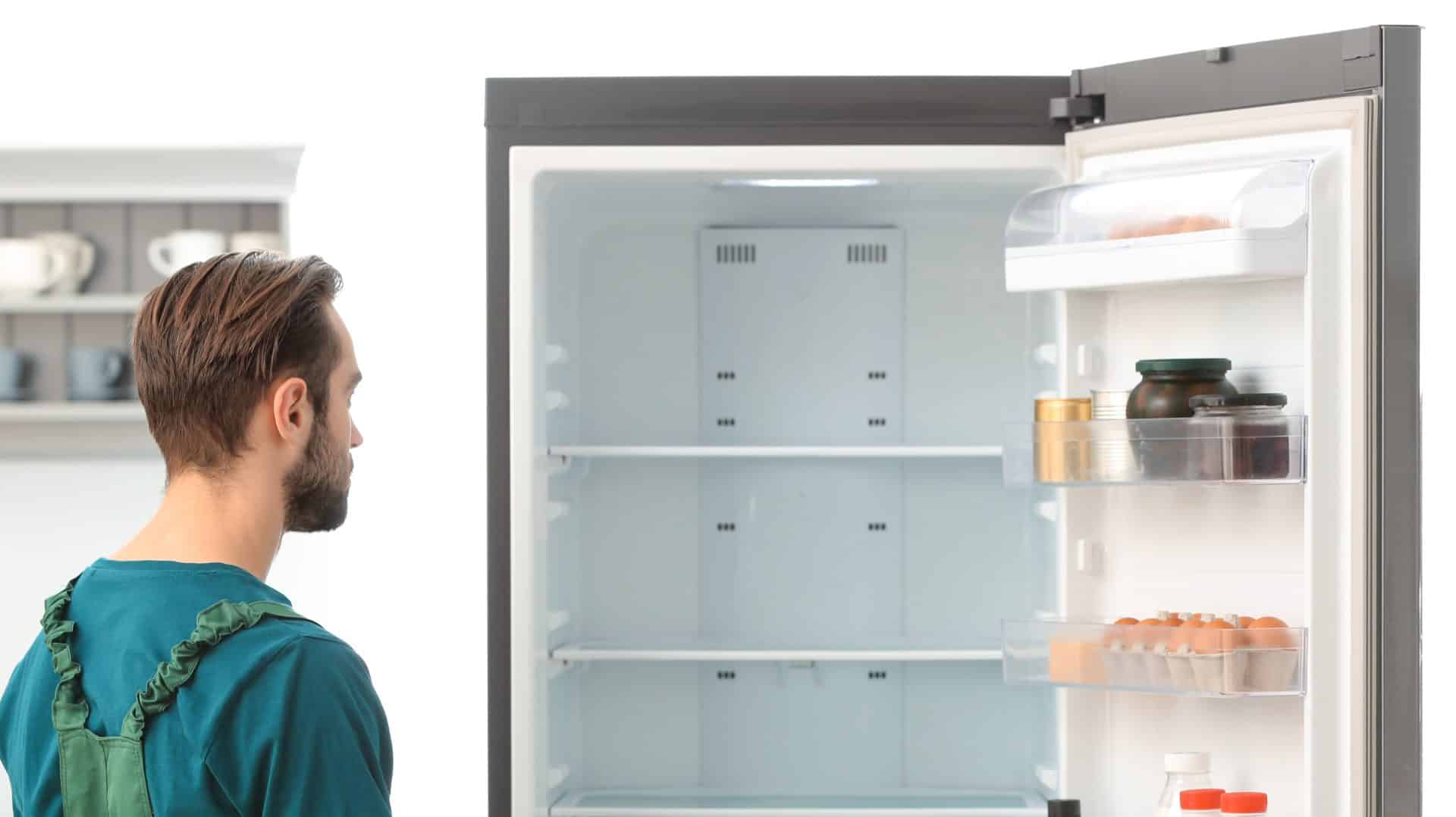 Male technician making notes during repair of refrigerator indoors