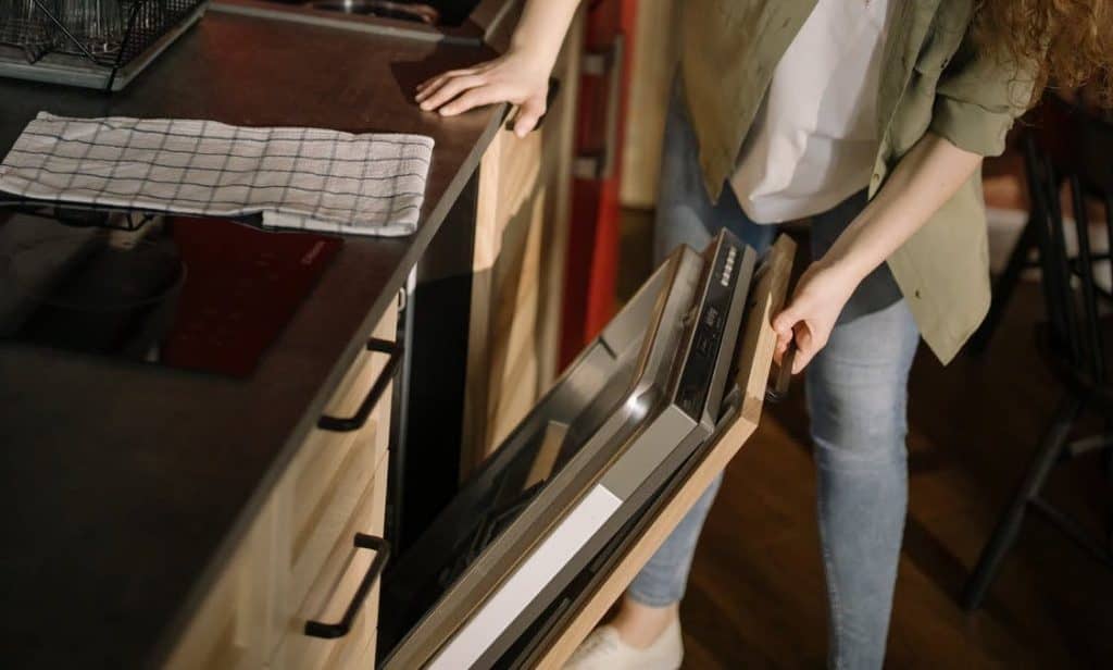 A woman holding the dishwasher door, trying to locate the screws to remove the panel