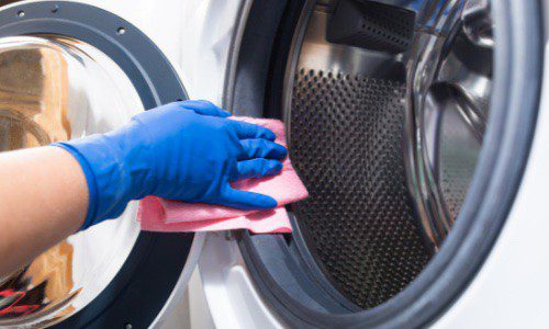 a hand wearing blue gloves cleaning the washing machine