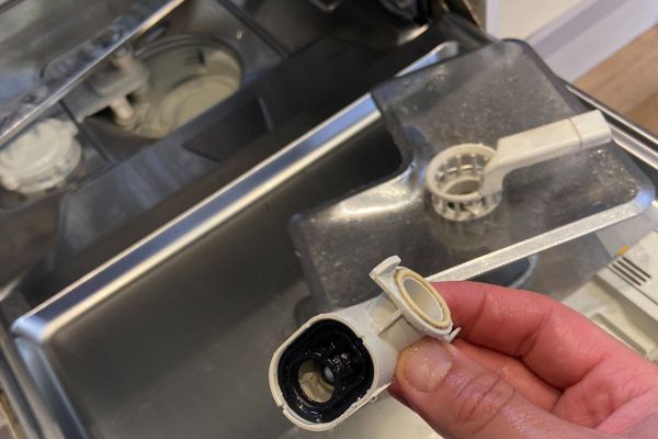 A close-up of a technicianโs hand holding a removed dishwasher spray arm part during a repair. The interior of the dishwasher is visible in the background, with components taken apart for servicing. This image highlights the hands-on diagnostics and repair work performed by Quality Appliance Repairs