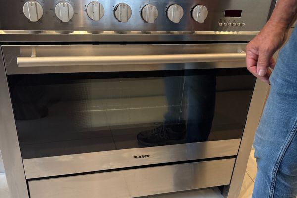 Technician from Quality Appliance Repairs inspecting a stainless steel oven during a professional onsite repair service.